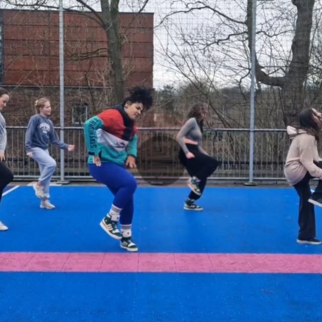 Mel en een groep dansen op een sportveld buiten